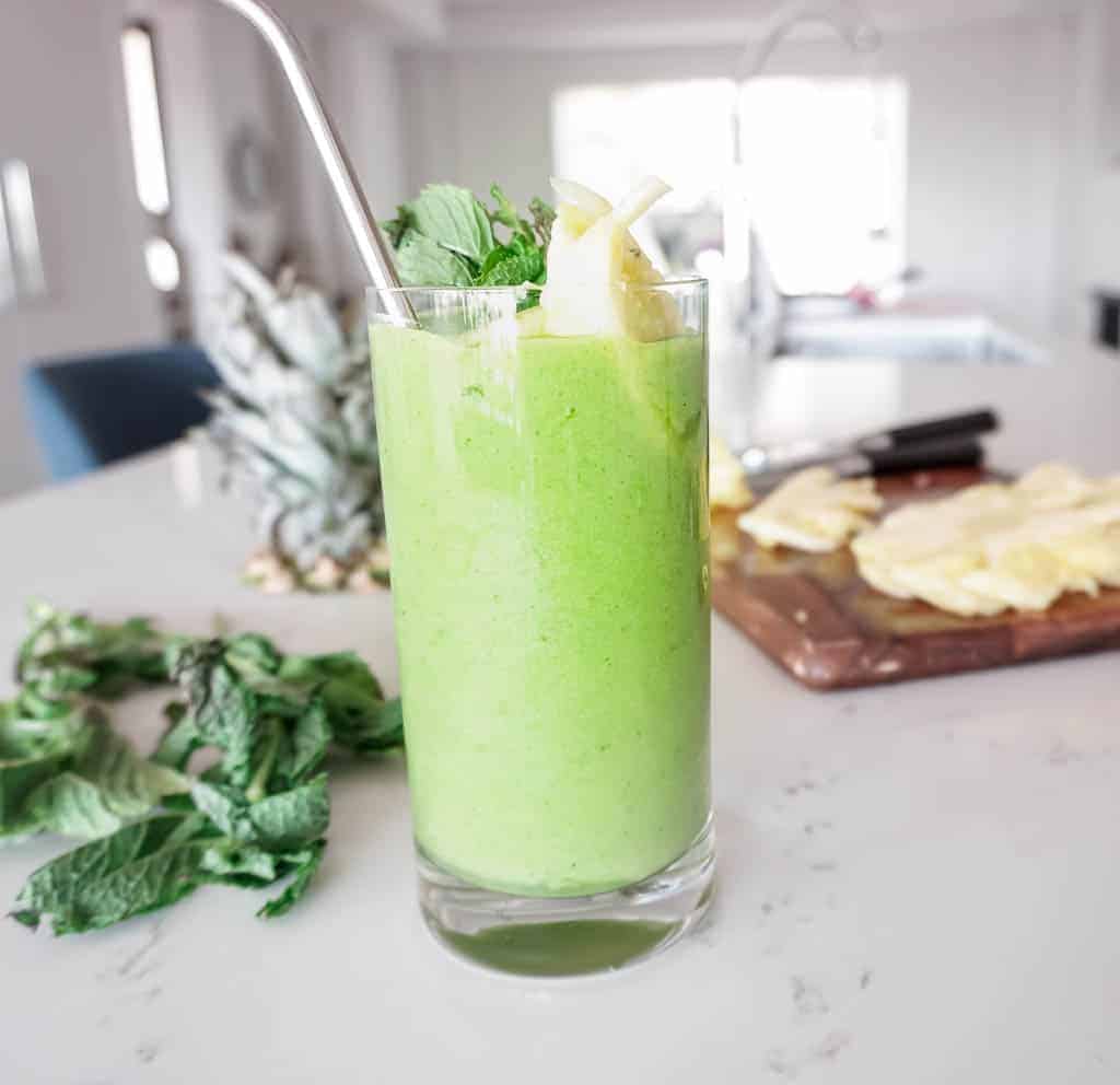 Image of a refreshing smoothie - with pineapple and mint sticking out of the glass with the green smoothie. Plus more pineapple and mint in the background.