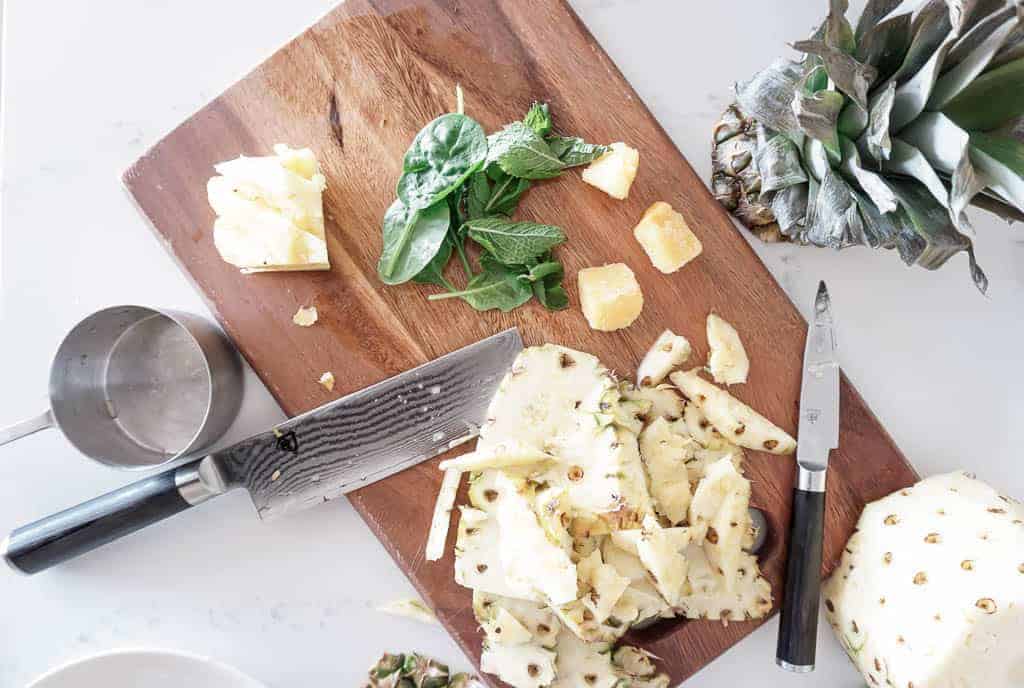 Image of the ingredients to make a refreshing pineapple mint smoothie. Includes chopped pineapple, mint leaves, and mango slices.