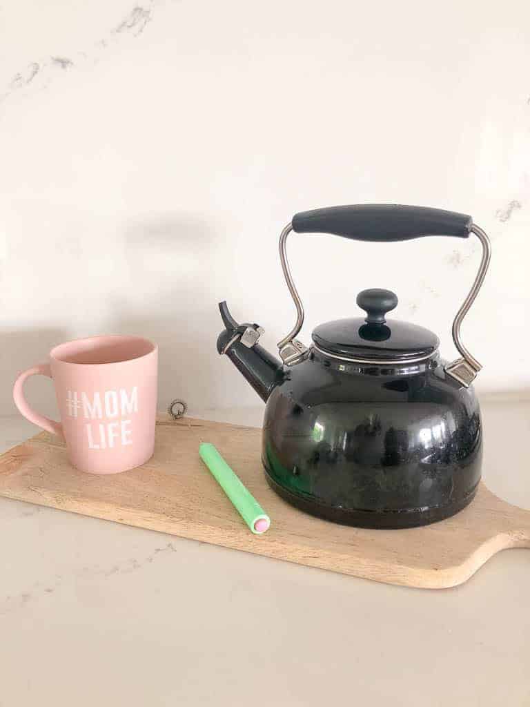 Tea Time with Signed Samantha - three items she recommends for the perfect tea time experience are sitting on a wood cutting board including an over-sized pink mug, a hand held milk frother, and a tea kettle.