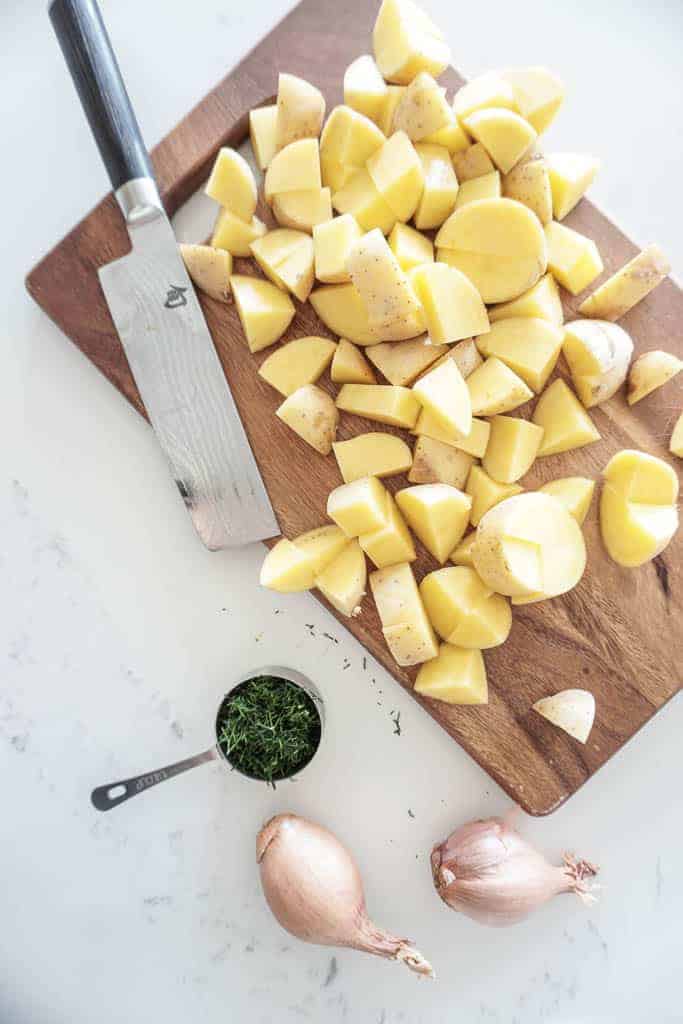 Signe Samantha's vegan potato salad. Diced potatoes on top of a cutting board with dill and shallots in the background.