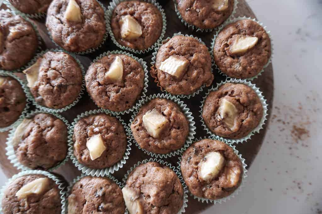 An overhead shot of Signed Samantha's Gluten Free Banana Mini Muffins. There are approximately 15 mini muffins pictured on a circular platter with little pieces of banana on top of each muffin.