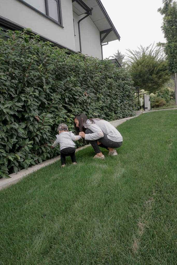 Signed Samantha and her daughter Sloane standing next to the bushes on the grass, exploring. Samantha is discussing what I've learned about motherhood