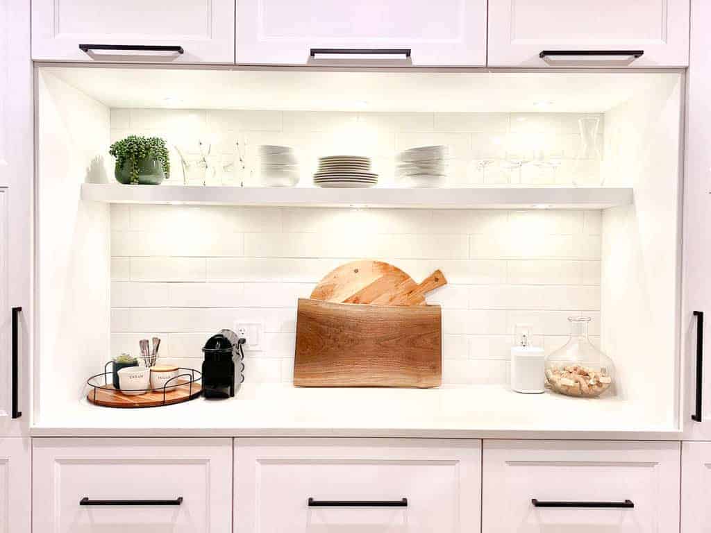 Signed Samantha's friend's kitchen countertop decor. She has a floating shelf with dishes and glasses above the counter which has two cutting boards, a coffee station and a speaker on it.