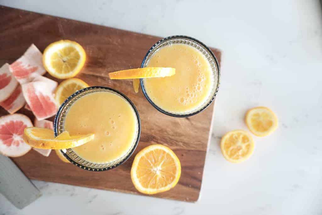 Signed Samantha's recipe for a wine smoothie. Two of the wine smoothies are pictured from overhead. Each has an orange sticking out of the glass. There are grapefruit and orange skins on the cutting board in the background