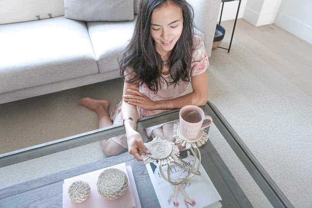 Signed Samantha is sitting on the ground leaning on the coffee table admiring her D.I.Y boho coasters that are made with macrame and have a fringe.