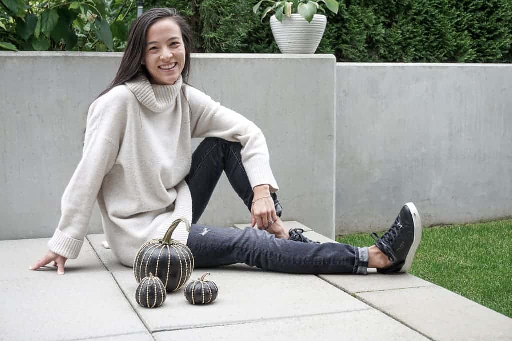 Signed Samantha sitting on the ground next to her black pumpkins that have rockstuds going from top to bottom around the pumpkin.