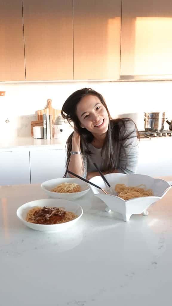 Short Rib Pasta Sauce pictured on a plate over spaghetti noodles There are two bowls beside this one and Signed Samantha is standing leaning on the counter behind the dishes.