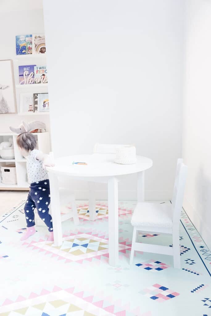 Sloane sitting on her new diy kids chair cushion at her kids play table which has paper and crayons on it.