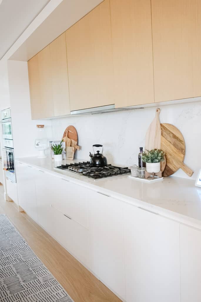 Signed Samantha's kitchen tour. White marble countertop, her stove is, then there are wooden cutting boards leaning against the back wall.