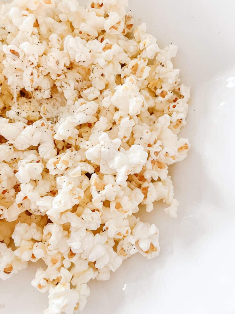 homemade popcorn toppings including parmesan, butter, and cracked pepper - pictured on the popcorn in a white bowl