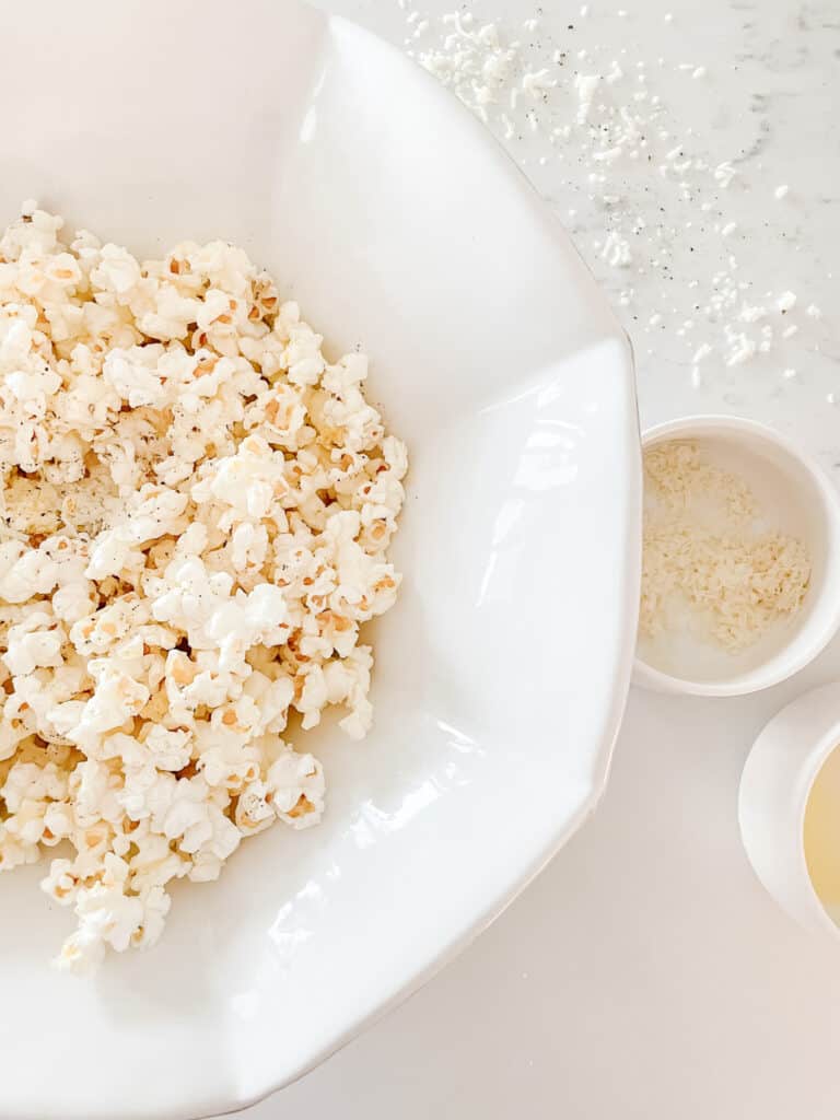 homemade popcorn toppings including parmesan, butter, and cracked pepper - pictured on the popcorn in a white bowl