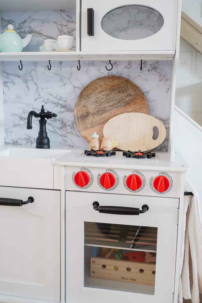 Signed Samantha Potter sharing her super simple way to do a kids kitchen makeover with her daughter, Sloane's kitchen. The kids kitchen that has red knobs, a faux marble backsplash, and black handles.