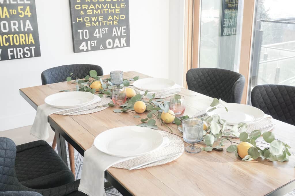 Signed Samantha sharing some home decor updates for spring including how to update your tablescape for this season. Pictured is her wood table with eucaylptus and lemons as well as neutral napkins and placemats, white plates and coloured glassware.