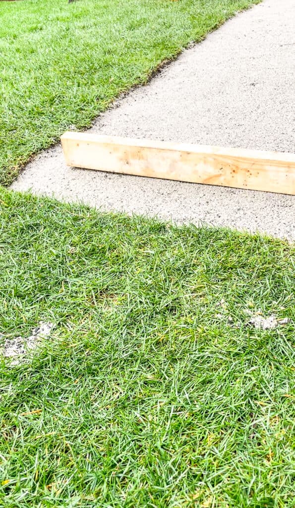 Signed Samantha explaining how to install patio paving stones using a 2x4 to level the sanded area - the 2x4 on top of the sand is pictured.