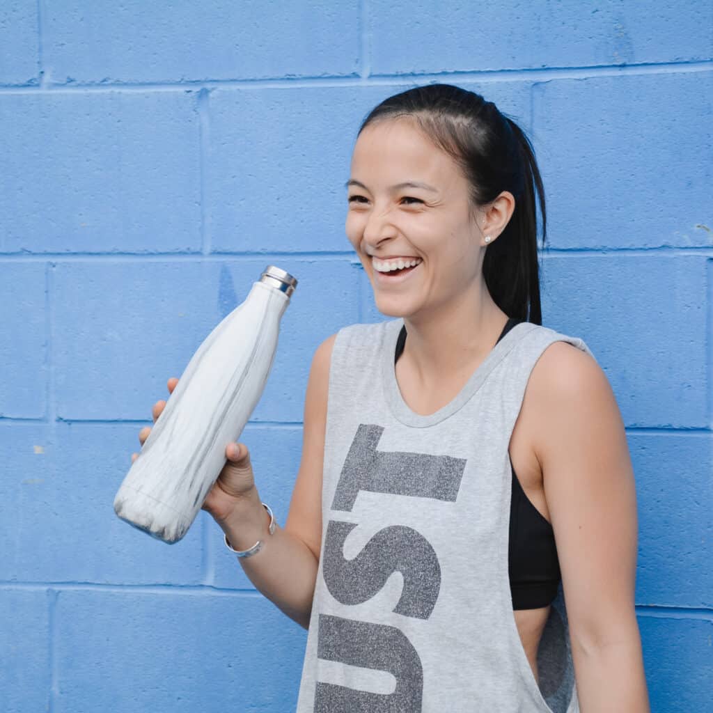 Self-Care during a pandemic includes working out. Samantha standing in a nike top drinking water after working out