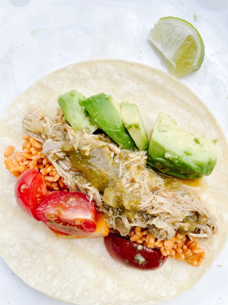 slow cooker chicken verde in a taco shell with rice, avocado, and tomatoes