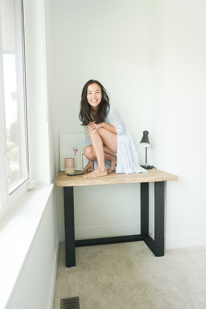 Signed Samantha sitting on top of her DIY desk with black legs that look like faux metal and a wood top