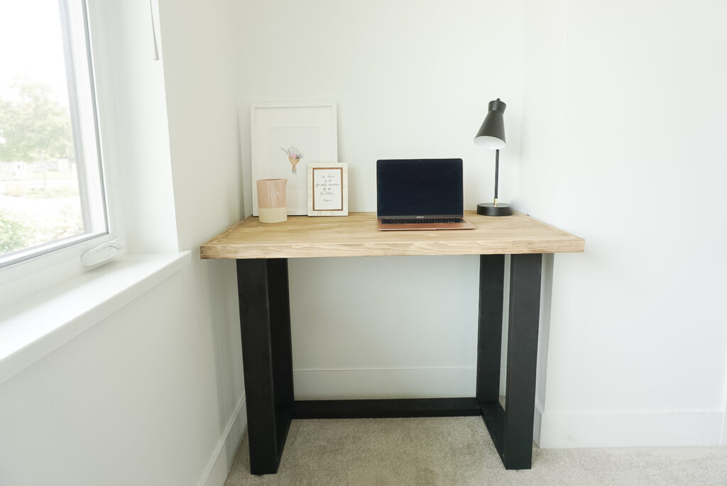 DIY desk sitting in the corner of the room the desk has black wood legs that look like metal and a wood table top