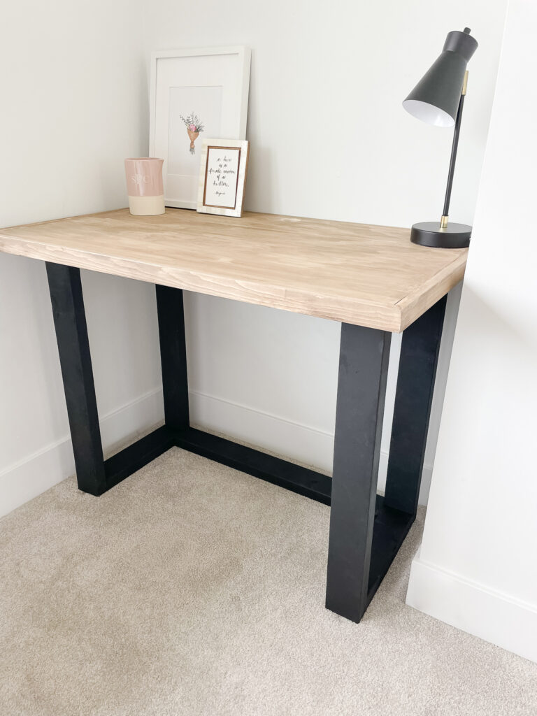 DIY desk sitting in the corner of the room the desk has black wood legs that look like metal and a wood table top