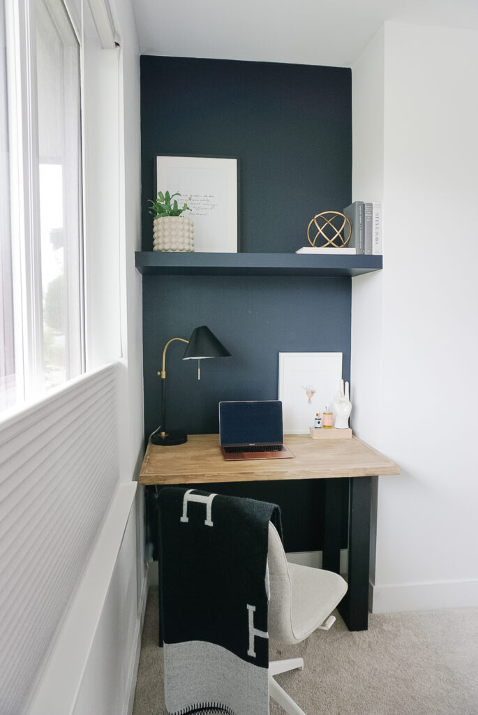 DIY floating shelf painted dark black with plants and art on top and a computer desk below.