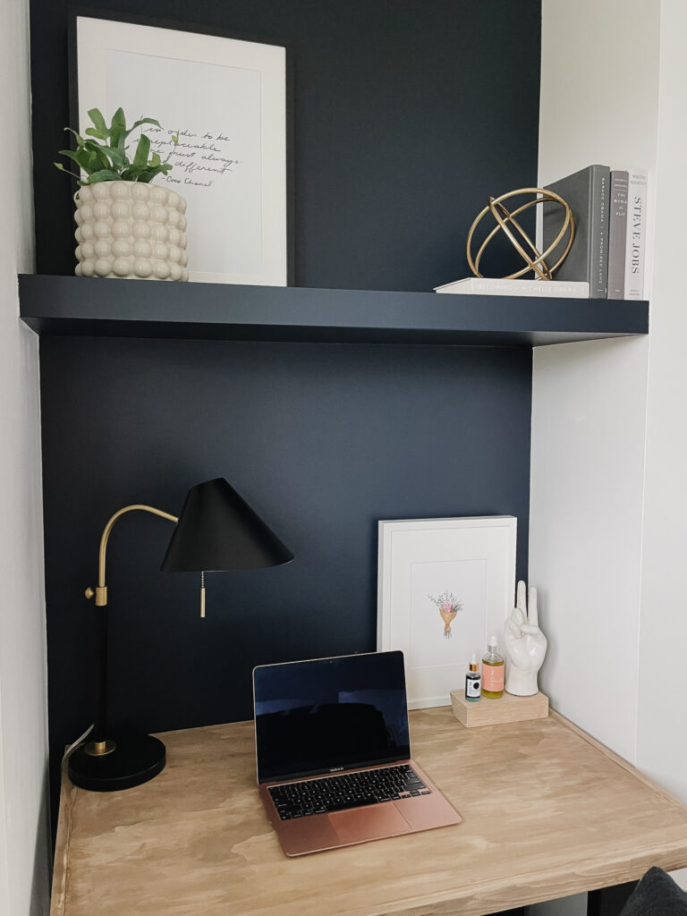 DIY floating shelf painted dark black with plants and art on top and a computer desk below.