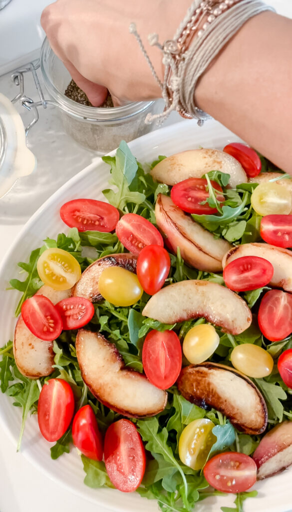 overhead shot of peach and burrata salad. The burrta is not yet on the salad but the peaches are on top of a bed of arugula along with cherry tomatoes