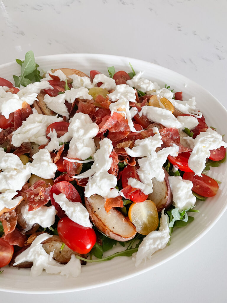 overhead shot of peach and burrata salad - there is burrata broken up on top the peaches which are on a bed of arugula.