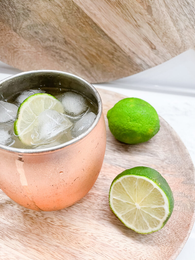 A smoked tequila mule in a copper mug with lime wedges.