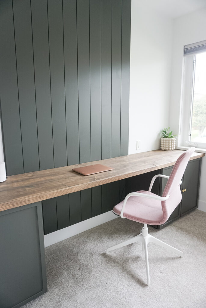 DIY Desk top for week 5 of the one room challenge - rusitc desktop, built in cabinets and a shiplap wall. Not yet done is a bookcase. There are small decor items on the desk and a pink chair.