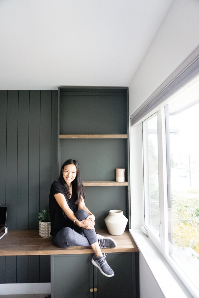 Signed Samantha sitting in front of her newly built-in bookshelf - not quite done but almost there in green with wood shelves.