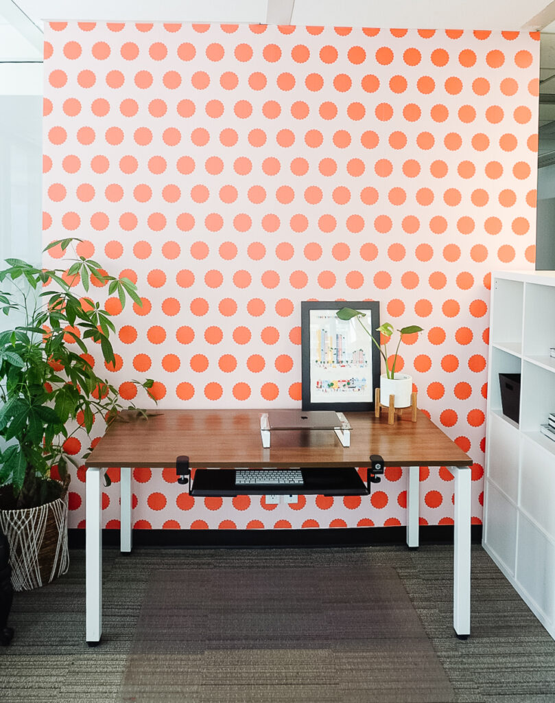 Otto studio's peel and stick wallpaper in polka pop - tangerine is on the wall with a desk and laptop in front.