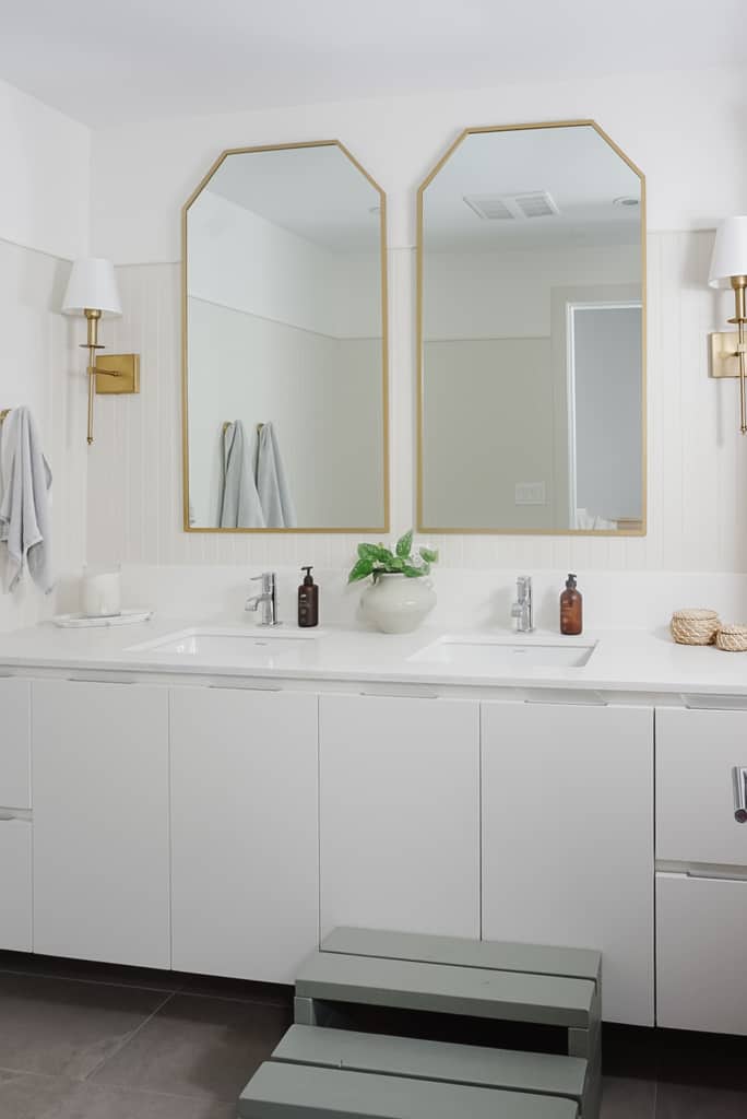 builder grade bathroom gets an upgrade with two gold mirrors, gold sconces, beadboard on the walls with a creamy white.