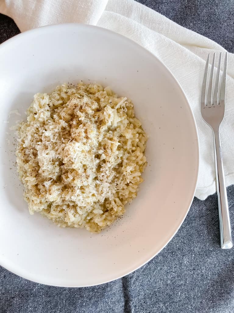 herb lemon instant pot risotto pictured in a white bowl with a fork and a dark grey napkin on the table around it.