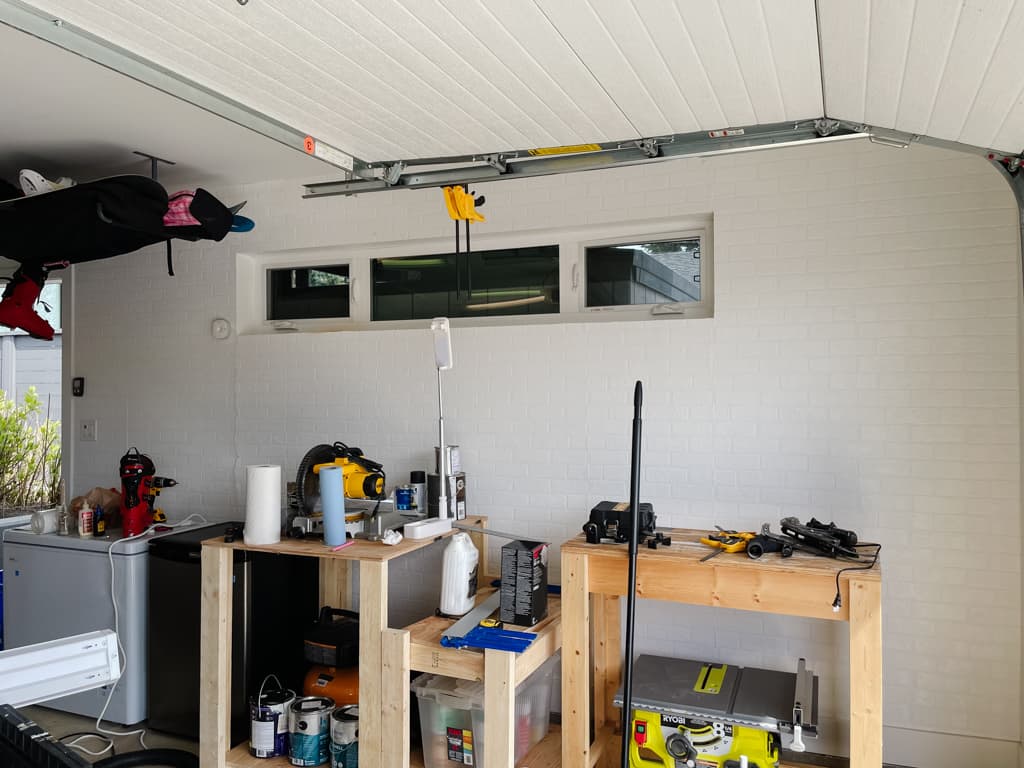 faux brick wallpaper walls in white brick - it looks so realistic - with a huge mess of random garage items in front of it - tools, incomplete work benches, etc.