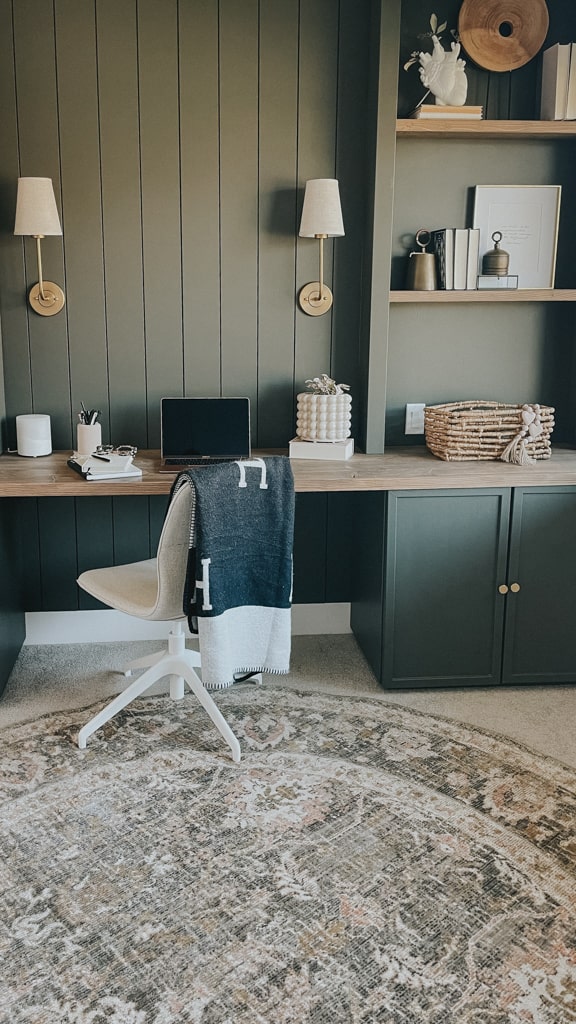 green home office with cabinets on the ground, a bookshelf above and a desktop in between. the green is a rich mossy green that compliments the cream of the office chair.