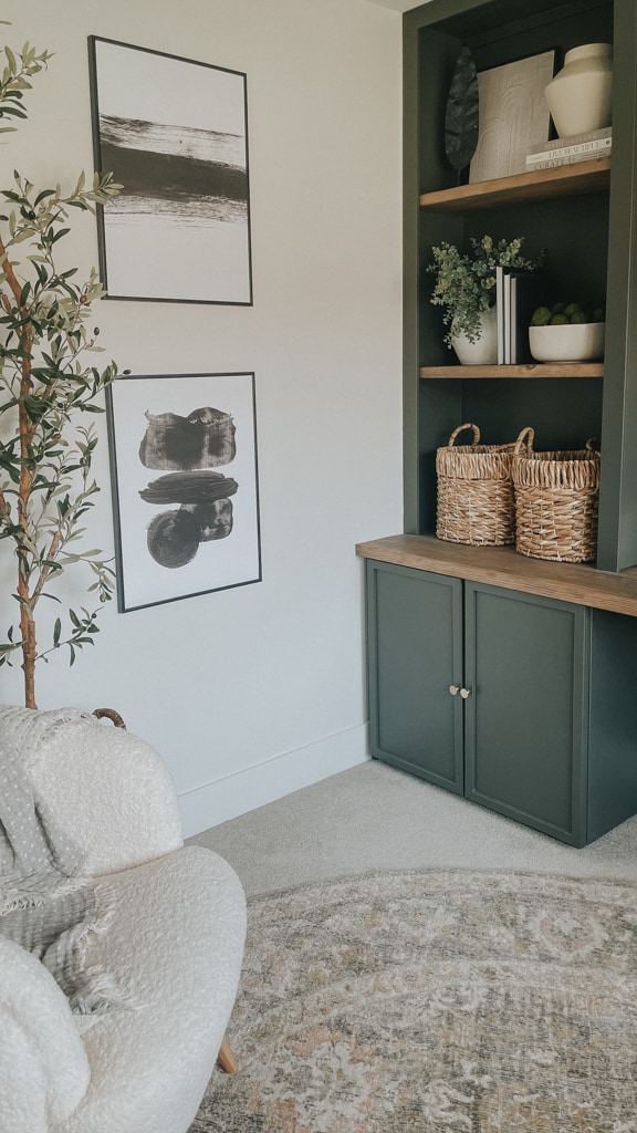 green home office with cabinets on the ground, a bookshelf above and a desktop in between. the green is a rich mossy green that compliments the cream of the office chair. black and white abstract art on the wall