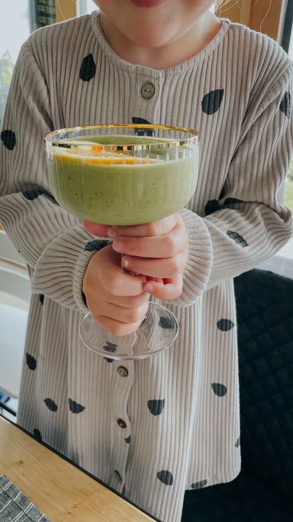 little girl holding up a green smoothie