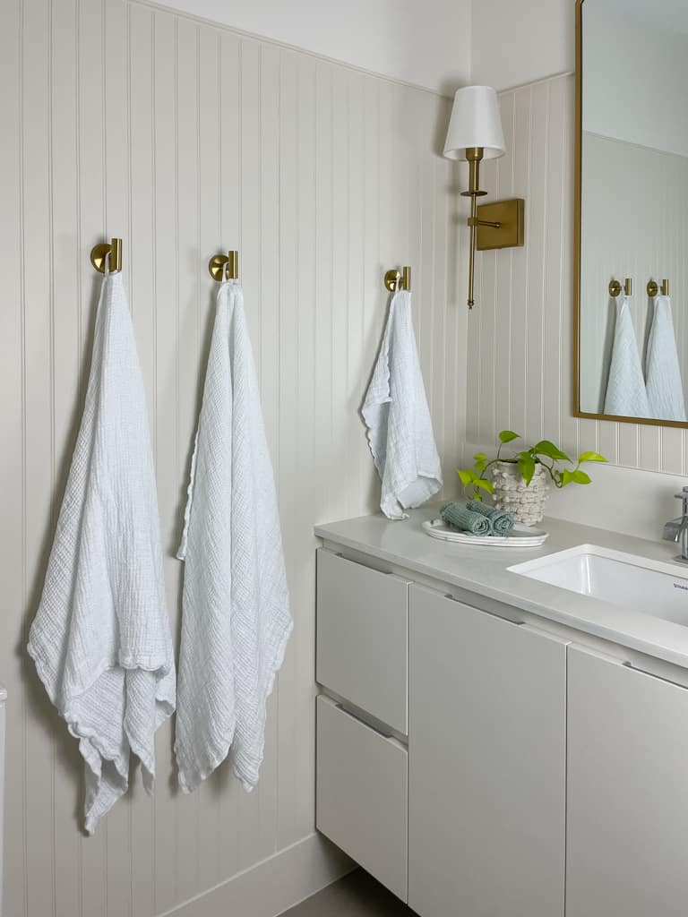 Flax Home linen waffle towels hanging up on gold hooks in a bathroom that has beadboard and a gold mirror