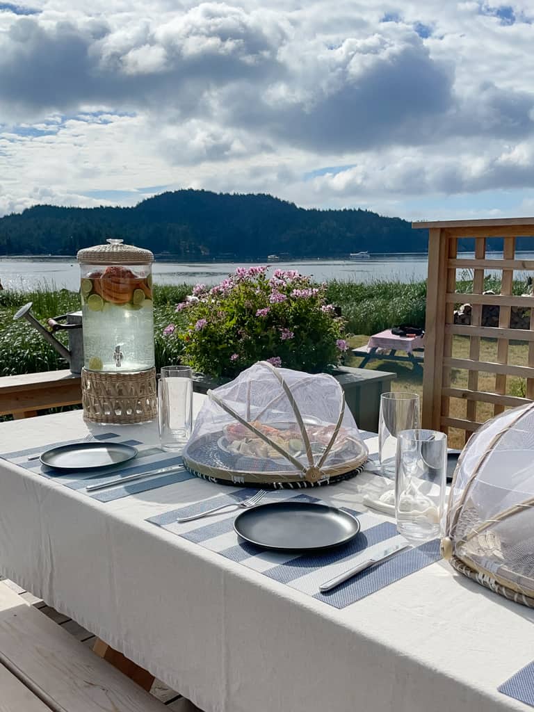 a perfect set up for outdoor enteratining. a picnic table with food under food nets and a drink dispenser