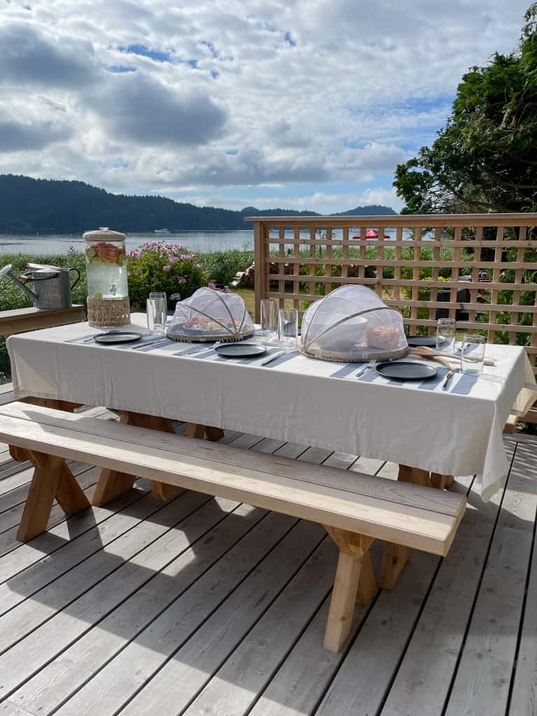 a perfect set up for outdoor enteratining. a picnic table with food under food nets and a drink dispenser