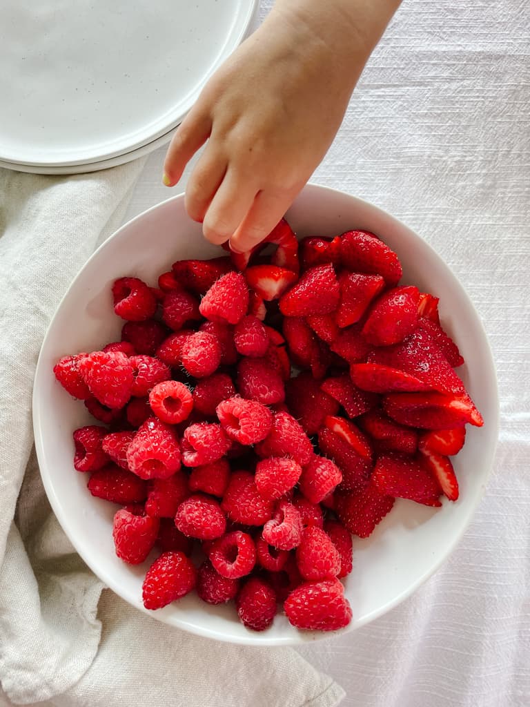 fable dishes filled with berries and a childs arm reaching to get some strawberries