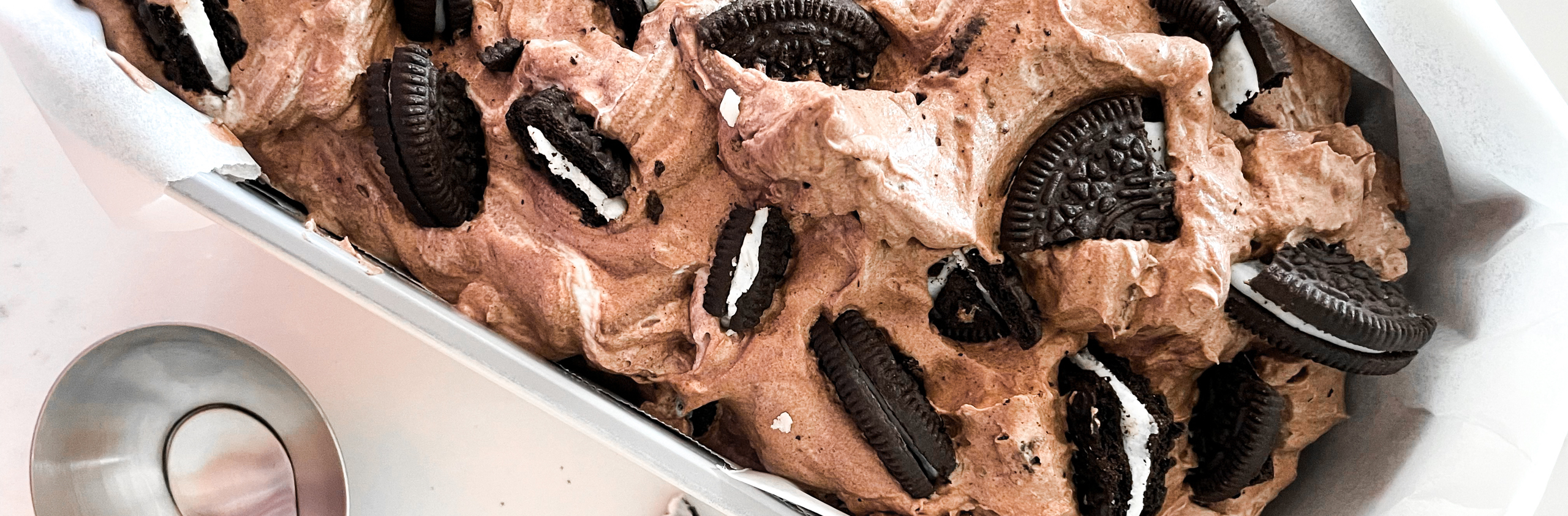 chocolate oreo ice cream pictured in a loaf pan with an ice cream scoop next to it