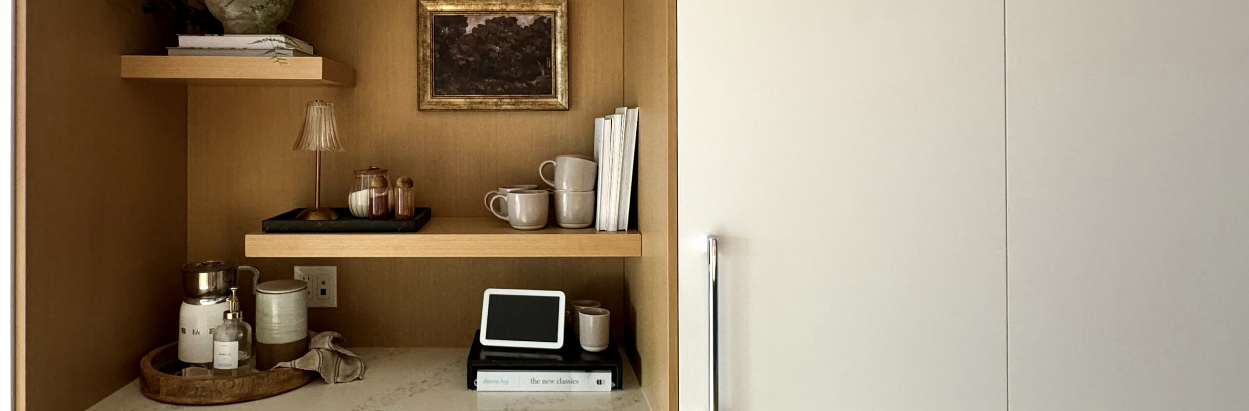 Tea bar decor with a milk frother, tea mugs, cook books, a lamp, cinnamon shaker, and more