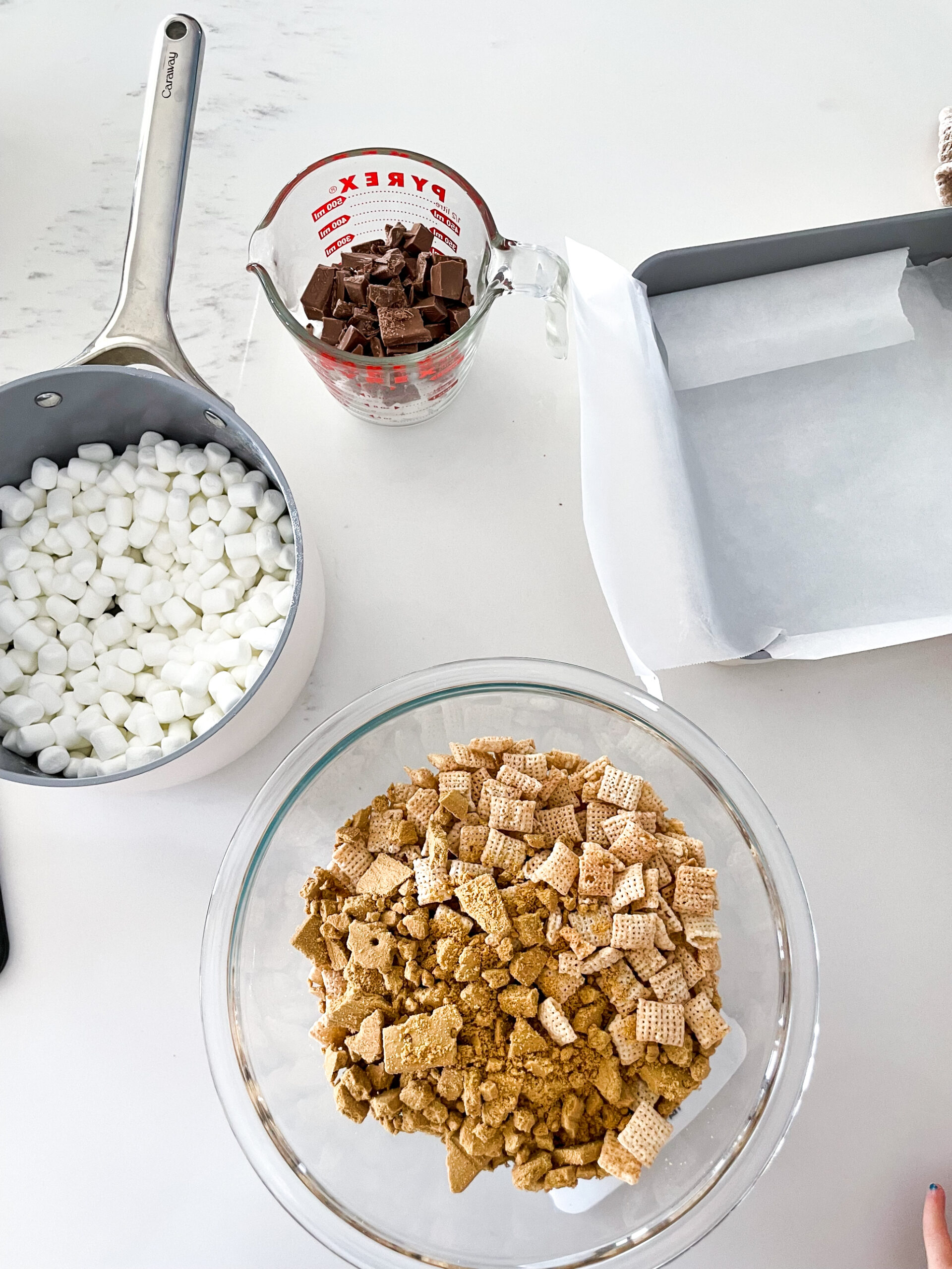 s'more krispies in the making with marshmallows in a pot, chocolate, and graham crackers and chex rice risps in a bowl.