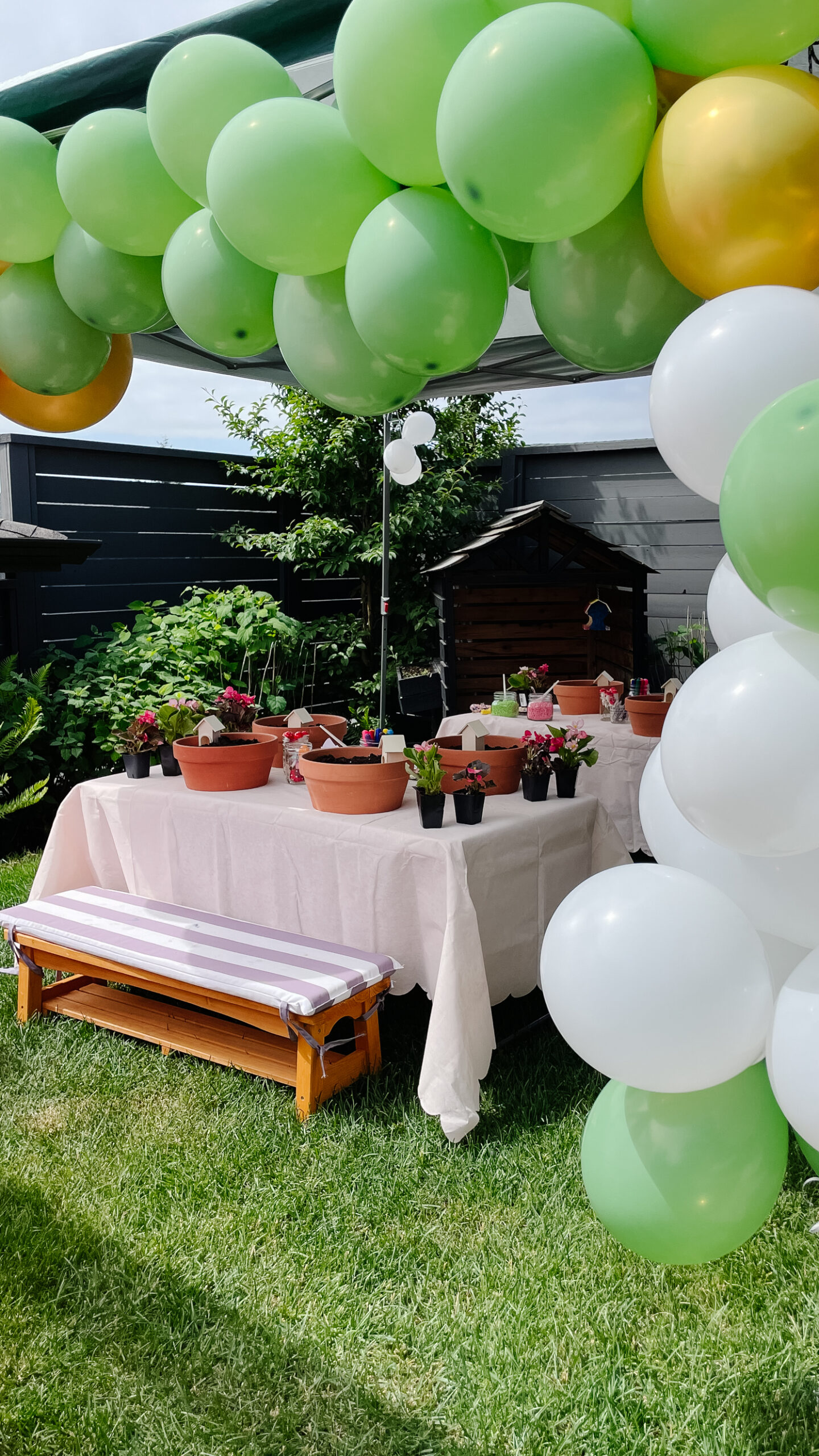 a fairy garden birthday party set up with balloons, picnic tables and chairs, and fair gardens to make