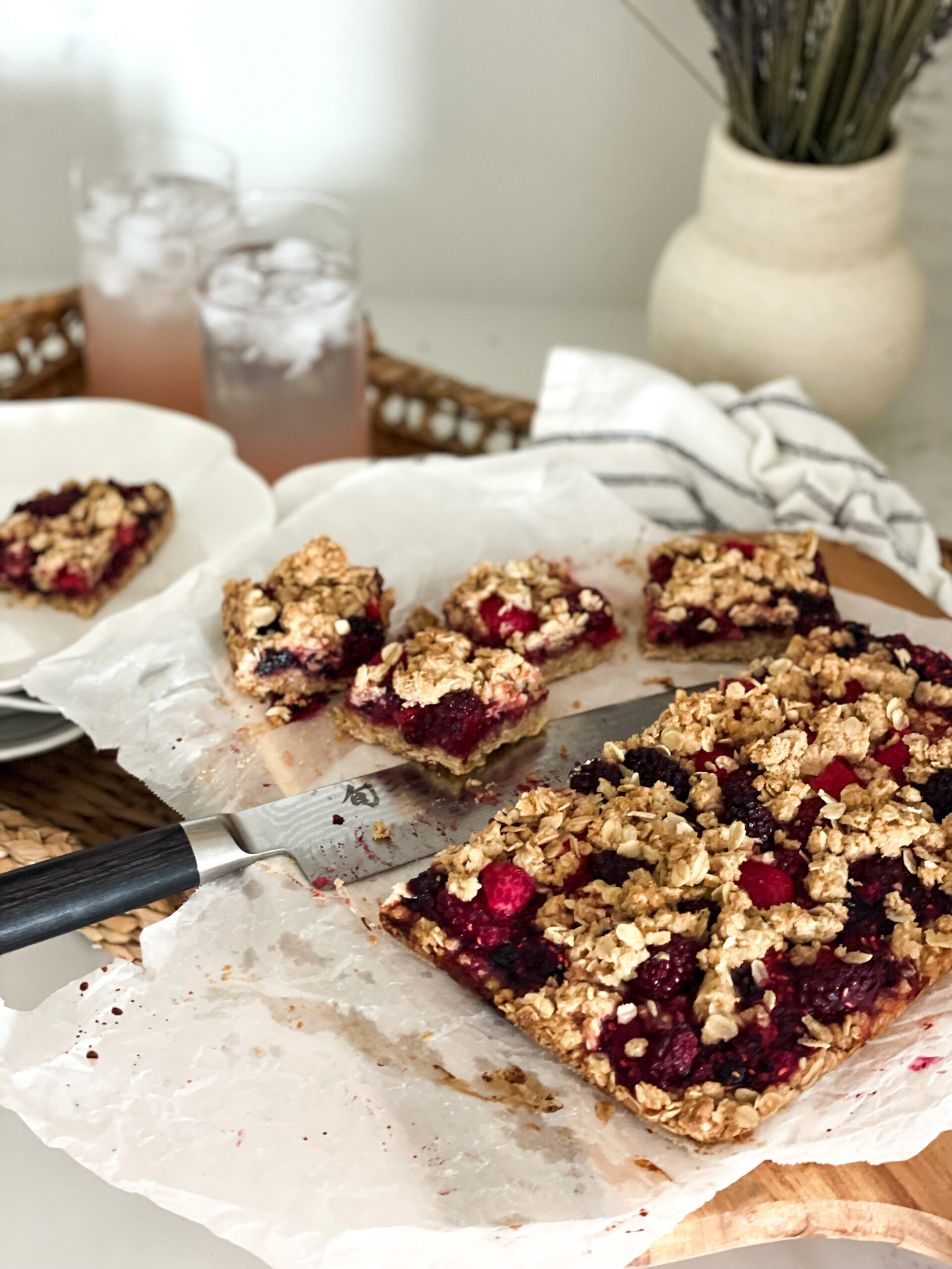 Brown Butter Berry Crumble cut up. Two pieces are sitting on a plate and the rest is on the cutting board with a knife