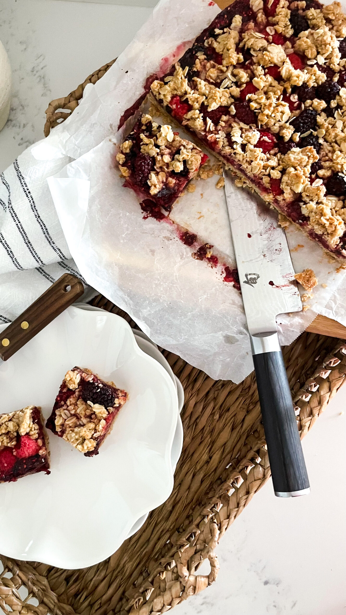 Brown Butter Berry Crumble cut up. Two pieces are sitting on a plate and the rest is on the cutting board with a knife