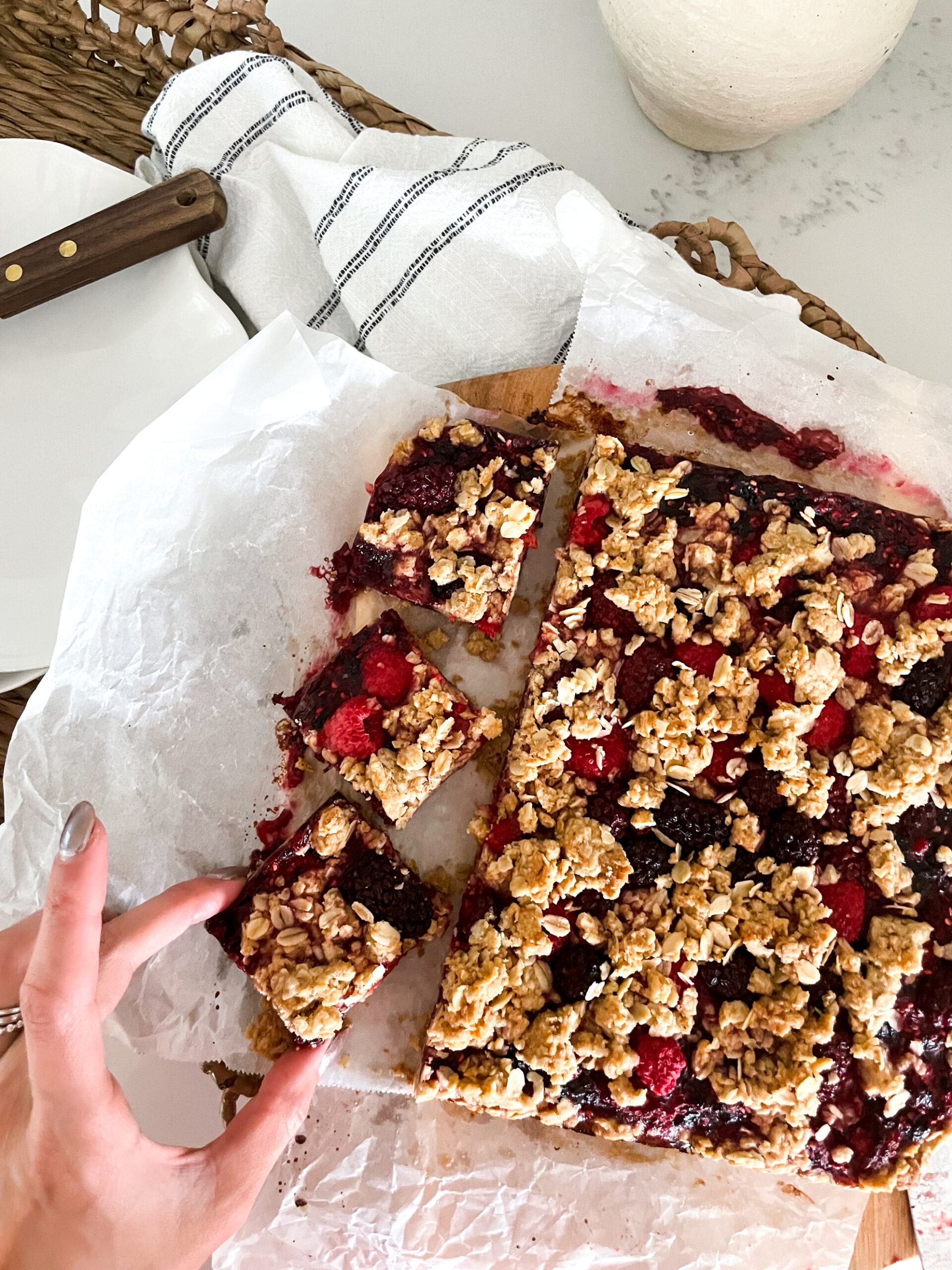 grabbing a piece of Brown Butter Berry Crumble from a cutting board. Beautiful red berry colours and a golden brown top