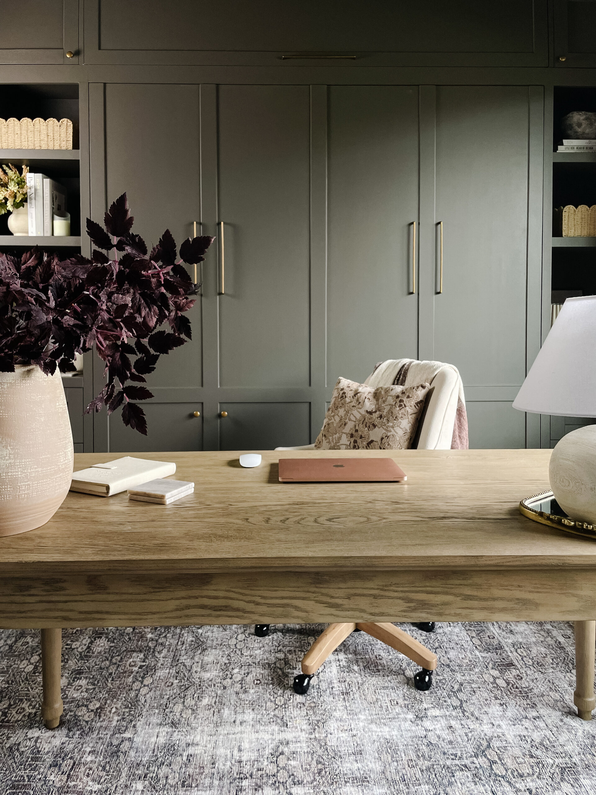 home office and guest room pictured is the home office space with a wooden desk, office chair, and dark green/bronze cabinetry behind