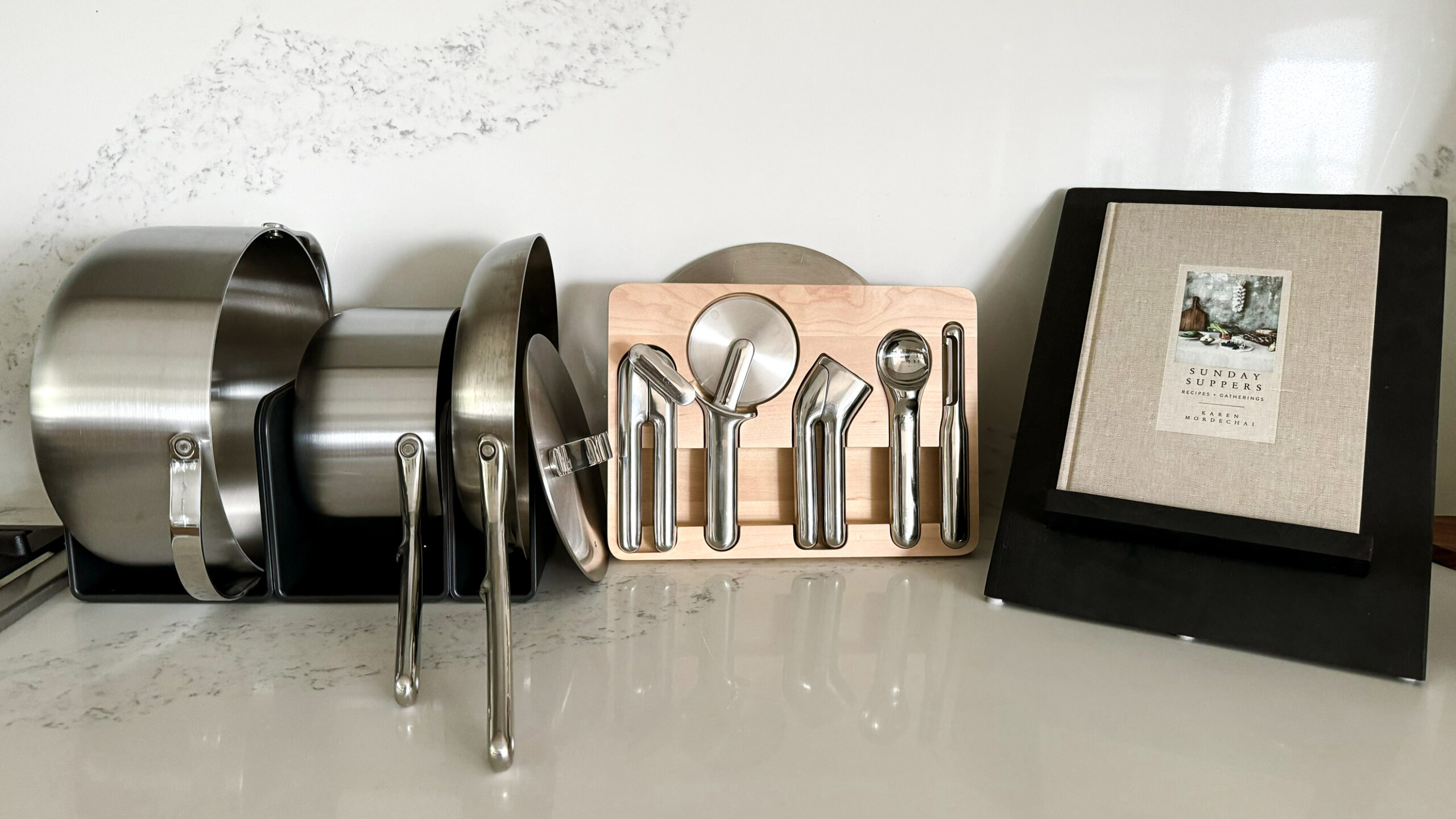 A review of Caraway's stainless steel set that is sitting on a kitchen counter in the magnetic organizers Caraway products come with, plus their new stainless kitchen gadgets sitting on the counter.